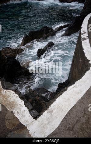 Wellen brechen an den natürlichen Pools von Porto Moniz unter einer scharfen Betonkante gegen vulkanische Felsen Stockfoto