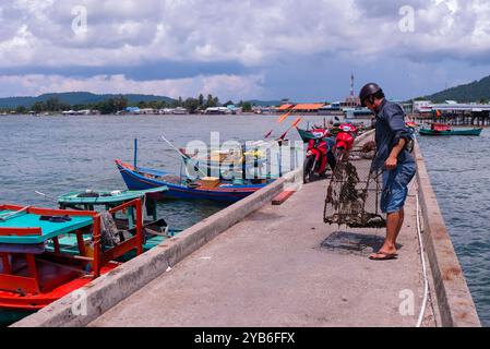 Phu Quoc, Vietnam 2018 Mai 17 Einheimischer sammelt seine Metallfischkäfigfalle am Steg in Ham Ninh Fishing Village an sonnigen Tagen. Fischerboote angedockt. Stockfoto