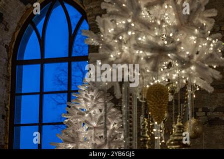 Weißer weihnachtsbaum mit funkelnden Lichtern steht am Fenster in einem Steinhaus und schafft eine gemütliche und festliche Atmosphäre Stockfoto