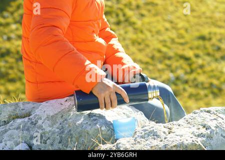 Ein Mann gießt Tee aus einer Thermoskanne, während einer Bergrestpause, Nahaufnahme. Outdoor-Erholung an einem Herbsttag: Ein Tourist, der auf einem Felsen sitzt, gießt ein Getränk Stockfoto