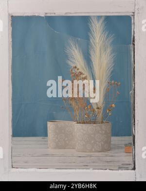 Boho-Dekoration in Holzfensterrahmen. Das Glas hat Risse. Leere Stelle zum Füllen mit Inhalt. Blauer Vorhang, Holztisch. Stockfoto