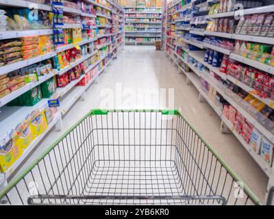 Leere rote Warenkorbansicht mit warmem Licht, Einkaufswagen im Supermarkt, Trolley im Kaufhaus abstrakte Unschärfe der bunten Regale. Stockfoto