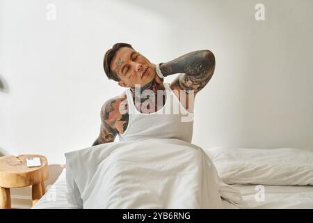 Ein hübscher junger Mann wacht zu Hause auf und dehnt sich bequem im Bett an einem ruhigen Morgen. Stockfoto