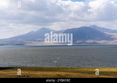 Gepflügtes Feld am Rande des Sees Paravani. Niedrige Wellen auf dem Wasser. Berge, Hügel, blauer Himmel mit Wolken im Hintergrund Stockfoto