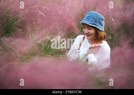 Glückliche schöne asiatische junge Frau umgeben von rosafarbenen Haaren muhly Gras (muhlenbergia capillaris) Stockfoto