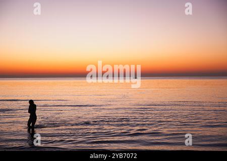 Frau, die beim Sonnenaufgang am Strand von Finikoudes in Zypern aus dem Meer kommt Stockfoto