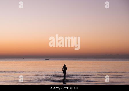 Frau, die beim Sonnenaufgang am Strand von Finikoudes in Zypern aus dem Meer kommt Stockfoto