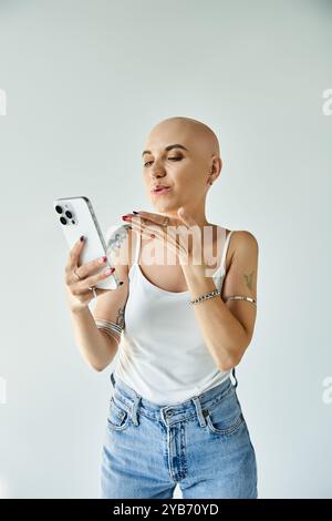 Eine kahlköpfige junge Frau strahlt Selbstvertrauen aus, während sie ihr Handy überprüft und spielerisch posiert. Stockfoto