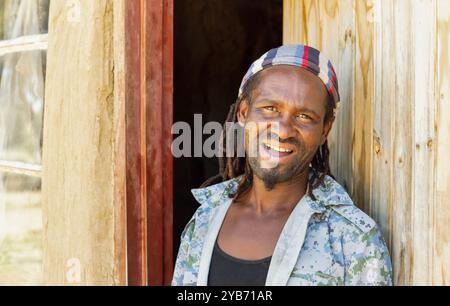 afrikanischer Dorfmann mit Dreadlocks, der vor dem Haus steht Stockfoto