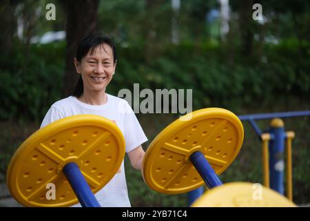 Eine glückliche alte asiatische Frau, die auf Fitnessgeräten im Freien trainiert. Blick auf die Kamera Stockfoto