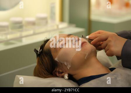 Asiatische junge Frau in Gesichtsmaske. Hautpflegebehandlung für Gesicht im Schönheitssalon Stockfoto