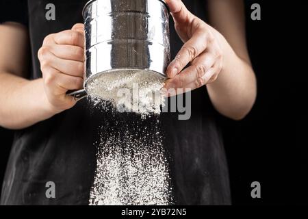 Der Koch siebt das Weizenmehl durch ein Metallsieb Stockfoto