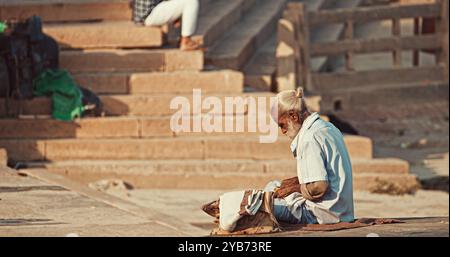 Varanasi, Indien. Der Alte Bettler Zählt Seine Einnahmen. Ein Alter Mann Sitzt Am Ganges Embankment. Der Senior-Mann Zählt Sein Geld. Vormittag Im Heiligen Varanasi Ghats Stockfoto