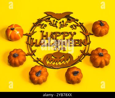 Dekoratives hölzernes Happy halloween Schild mit Fledermäusen und kleinen orangen Kürbissen auf gelbem Hintergrund, halloween Türdekoration, 31. Oktober Stockfoto