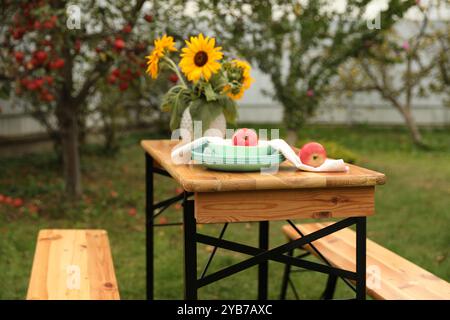 Äpfel und Vase mit Sonnenblumen auf Holztisch im Garten, selektiver Fokus Stockfoto