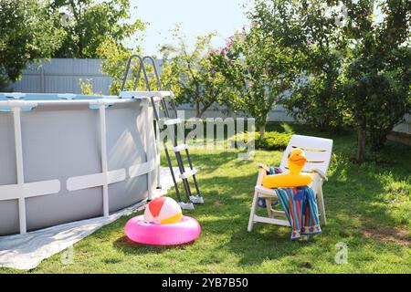 Oberirdischer Swimmingpool, Klappstuhl, Handtuch, aufblasbare Ringe und Ball im Hinterhof Stockfoto