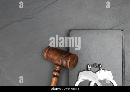 Buch, richterlicher Hammer und Handschellen auf grauem, strukturiertem Tisch, Draufsicht. Leerzeichen für Text Stockfoto