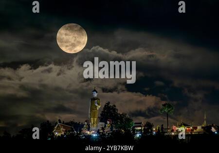 Chiang Mai, Thailand. Oktober 2024. Der Vollmond, der auf einer seiner nächsten Umlaufbahnen zur Erde gesehen wird, schwimmt in der Nähe der stehenden Buddha-Statue am Wat Phra That Doi Kham. Der Vollmond wird am nächsten zur Erde umkreisen, der als Supermond bekannt ist, wodurch der Mond größer und heller als sonst erscheint. Quelle: SOPA Images Limited/Alamy Live News Stockfoto