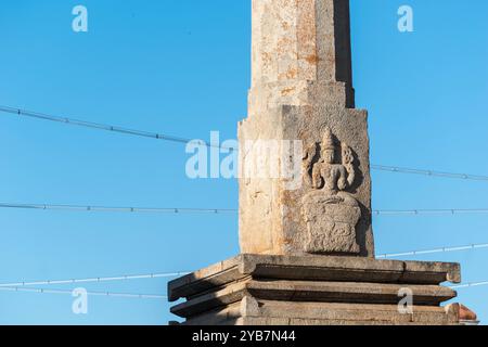 Dieses Bild zeigt eine detaillierte Steinschnitzerei eines Jain Tirthankara auf einer antiken Säule in der historischen Stadt Shravanabelagola, die vor einer ruhigen Kulisse liegt Stockfoto