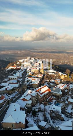 Ein atemberaubender Blick aus der Luft auf ein schneebedecktes Dorf auf einem Hügel in Georgia mit historischen Steinhäusern, Häusern mit roten Dächern und einem Kirchturm. Stockfoto