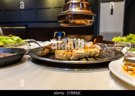 Seitenansicht des köstlichen koreanischen Grillgerichts mit Rindfleisch-, Schwein- und Hühnchenstücken, die auf Gitter zum Grillen gelegt werden, mit Gewürzen und Gemüse. Stockfoto