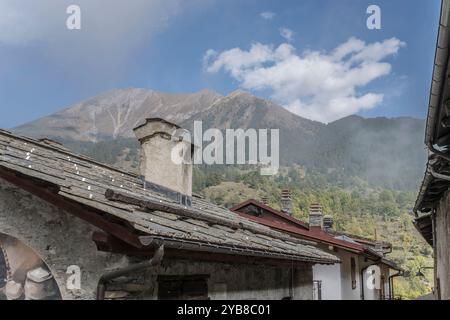 Stadtbild mit Schornsteintöpfen auf Schieferdach im historischen Bergdorf Valchisone Valley, im hellen Herbstlicht in Usseaux mit Pelvo Peak i aufgenommen Stockfoto