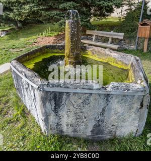 Stadtbild mit einem alten Steinbrunnen im Park im historischen Bergdorf Valchisone Valley, aufgenommen im hellen Herbstlicht in Usseaux, Turin, Italien Stockfoto