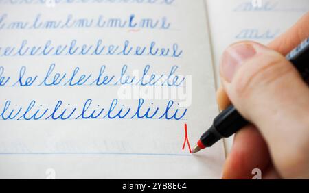 Nahaufnahme einer kaukasischen Hand, die rote Klasse eins unter blauen Buchstaben schreibt, geschrieben in Kursivschrift von einem Kind in einem linierten Notizbuch. Stockfoto