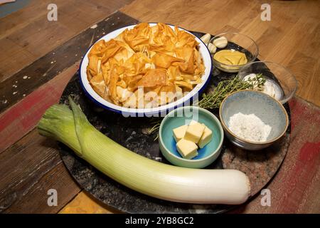 Ein köstlicher Hühnchen-, Lauch- und Wildpilzkuchen, umgeben von den Zutaten, die für die Zubereitung des Gerichts auf einem hölzernen Küchentisch verwendet werden Stockfoto