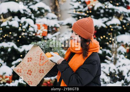 Junge Frau in hellen Winteraccessoires, die Weihnachtsdekoration und Geschenke trägt und den gemütlichen Minimalismus-Trend in der Wintermode und Weihnachtsdekoration widerspiegelt Stockfoto