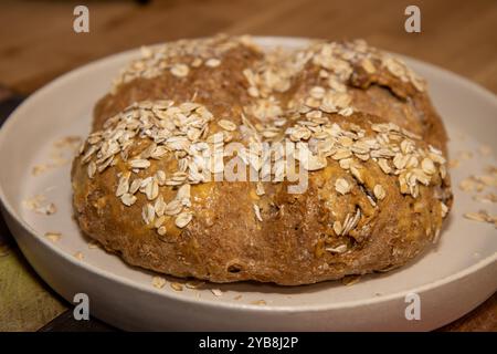 Ein rundes, selbstgebackenes Brötchen, bedeckt mit Samen auf einem weißen Teller Stockfoto