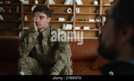 Verärgert depressive Verzweiflung kaukasischer männlicher Militärsoldat Veteran Tarnung Uniformoffizier mit Schmerz Kopf halten denken drinnen mit sitzen Stockfoto