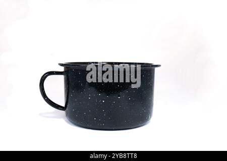 Ein beliebter alter alter alter alter, schwarz gefleckter Vintage-Becher wird oft auf einem Campingplatz gesehen und ist nützlich für Kaffee, Suppe, Wasser und vieles mehr. Wird auf weißem B angezeigt Stockfoto