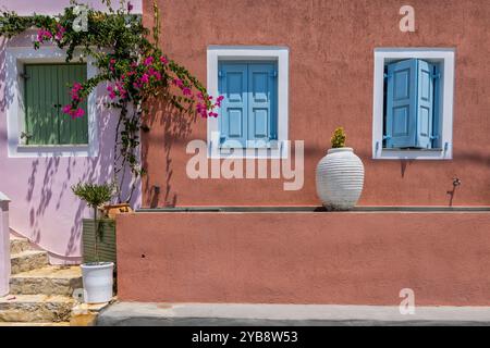 Ein bezauberndes Haus mit rosafarbenen Wänden in Assos, Kefalonia. Die hellblauen Fensterläden und die weißen Zierleisten bilden einen auffälligen Kontrast zur lebendigen Fassade. Rosa Stockfoto