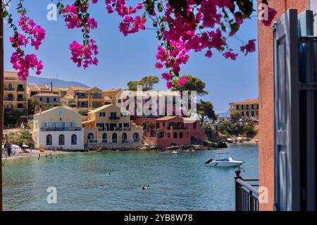 Ein malerisches Dorf in Assos, Kefalonia, Griechenland. Farbenfrohe Häuser säumen die Küste mit einem kleinen Hafen und Booten. Das Bild wird von leuchtendem Pink B eingerahmt Stockfoto