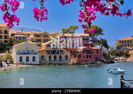 Ein malerisches Dorf in Assos, Kefalonia, Griechenland. Farbenfrohe Häuser säumen die Küste mit einem kleinen Hafen und Booten. Das Bild wird von leuchtendem Pink B eingerahmt Stockfoto