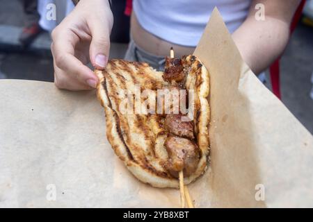 Eine Person hält ein gegrilltes Pita, das um einen Spieß gegrilltes Fleisch gewickelt ist. Das Gericht scheint ein traditionelles Street Food zu sein, mit der Pita und dem verkohlten Stockfoto