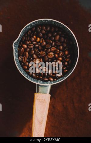Blick von oben auf die Kaffeekanne mit Holzgriff, in die geröstete Kaffeebohnen gestellt werden, und die Kaffeekanne steht auf dem gemahlenen Kaffee. Stockfoto