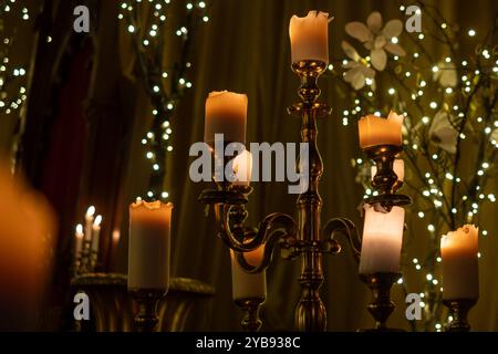 Ein Vintage-Kandelaber mit beleuchteten Kerzen steht elegant in einem warm beleuchteten Raum, umgeben von funkelnden Lichtern und floralen Dekorationen Stockfoto