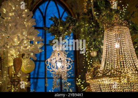 Ein eleganter Kronleuchter hängt anmutig zwischen festlichen Dekorationen, mit funkelnden Lichtern, die den Raum während eines gemütlichen Feiertags erleuchten. Stockfoto