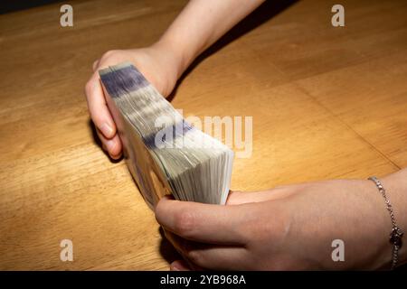 Eine Person, die einen dicken Stapel Bargeld mit einem hölzernen Tischhintergrund hält. Das Bargeld ist ordentlich angeordnet und zeigt verschiedene Stückelungen. Die Hände sind in Position Stockfoto