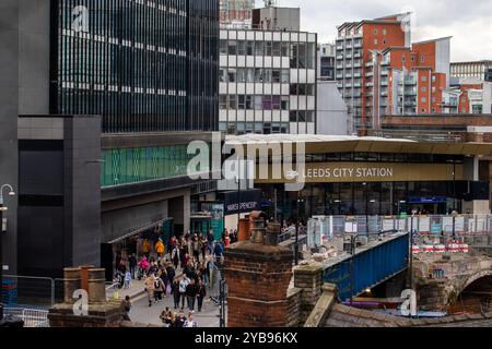 Eine geschäftige Straßenszene vor dem Bahnhof Leeds City mit einer Menschenmenge, die am Eingang vorbeiläuft. An der Stationsfassade befindet sich ein großes Schild mit Stockfoto