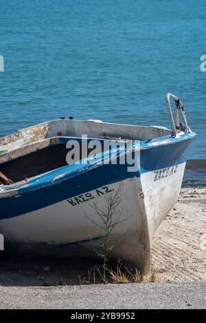 Altes Holzboot oder Ruderboot, das an einem sonnigen Tag an einem mediterranen Strand angespült wurde. Stockfoto
