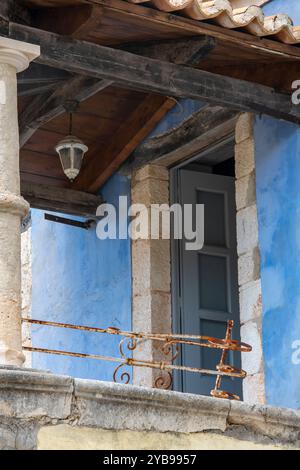 Offene Tür auf einem rostigen alten Balkon in einem rustikalen Landhaus in Griechenland. Schäbiges, schickes, heruntergekommenes Haus, gemalt in abblättriger Pulverblaufarbe Stockfoto
