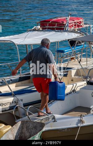 Mann, der einen schweren Wasser- oder Treibstoffbehälter auf seinem Boot in einem mediterranen Yachthafen trägt. Stockfoto