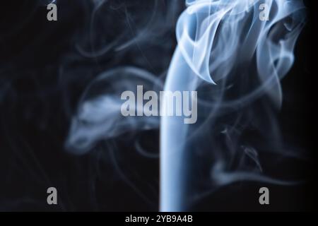 Ein zarter Rauchwirbel erhebt sich anmutig vor einem dunklen Hintergrund und schafft faszinierende Formen, die ein Gefühl von Ruhe und myst hervorrufen Stockfoto