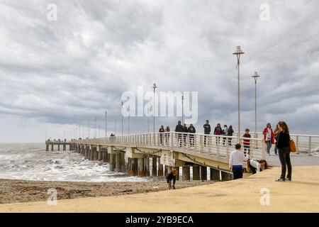 Menschen gehen an einem bewölkten Frühlingstag auf dem Pier der Küstenstadt, Marina di Massa, Massa Carrara, Toskana, Italien Stockfoto