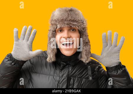 Junger Mann in schwarzer stilvoller Pufferjacke und Hut auf gelbem Hintergrund Stockfoto