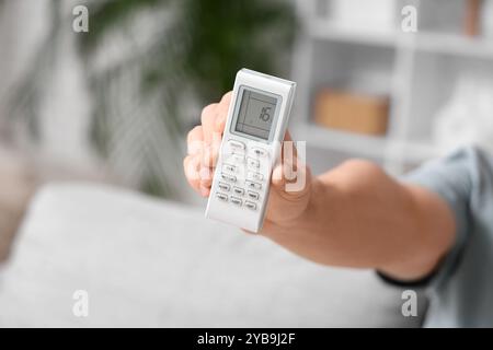 Junger Mann, der die Fernbedienung der Klimaanlage zu Hause zeigt, Nahaufnahme Stockfoto