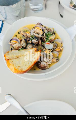 Muscheln in Brühe im Restaurant mit Sauerteigbrotscheiben, weißer Schüssel Stockfoto
